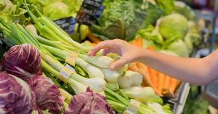 Someone reaching for a vegetable in the produce section of a store. 
