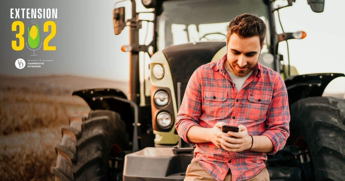 A farmer standing in front of his tractor looking at his phone