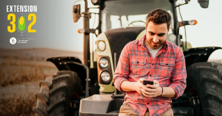 A farmer standing in front of his tractor looking at his phone
