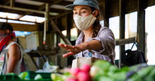 A produce worker reaching for a fruit wearing a mask