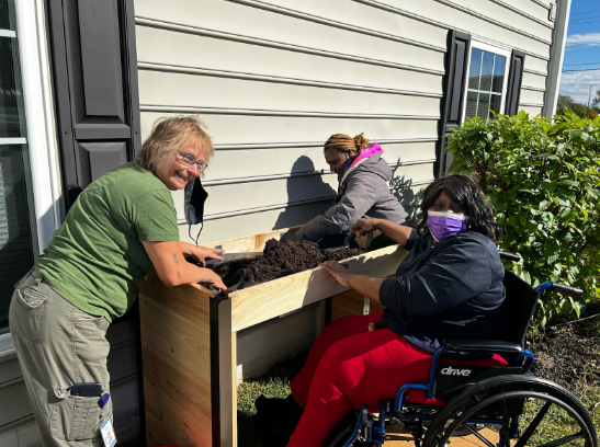 A few adults working with some soil next to the exterior of a home.