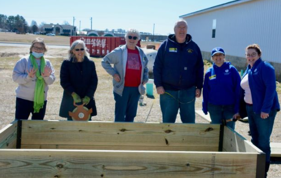 A group of adults poses and smiles outside near a trough of soil.