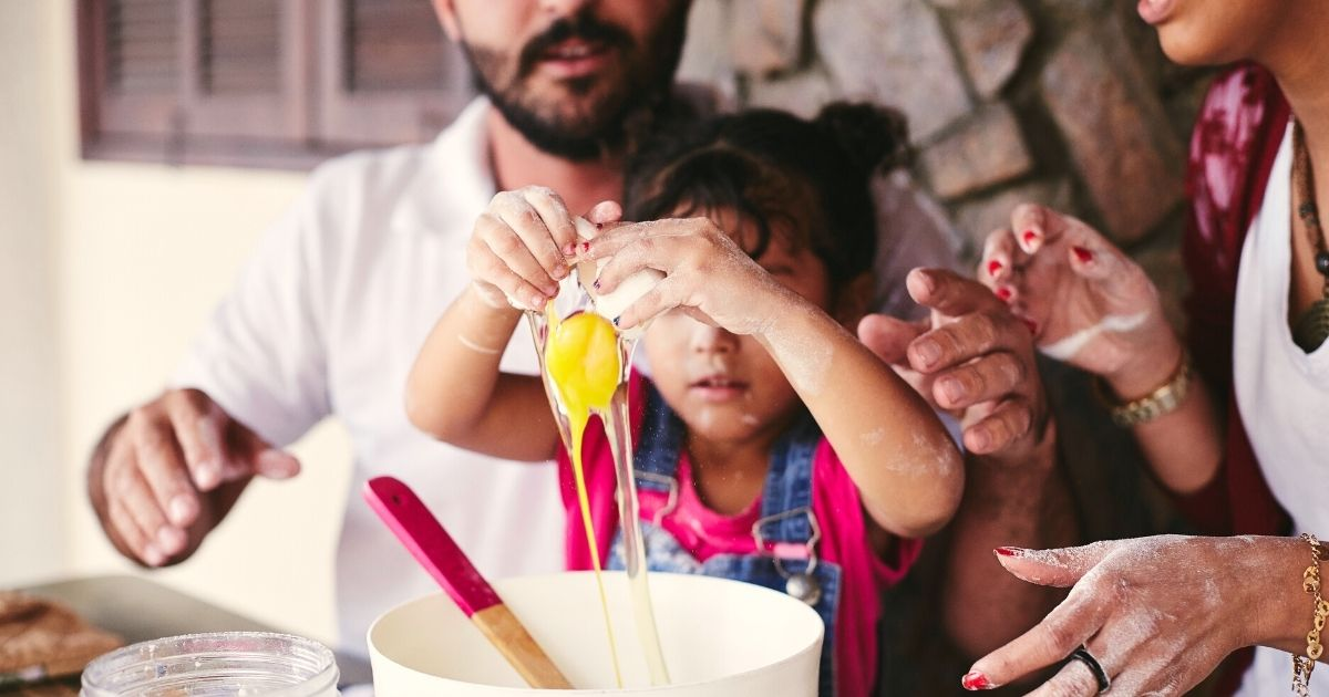 A photo of parents cracking an egg with their child