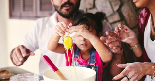 A photo of parents cracking an egg with their child