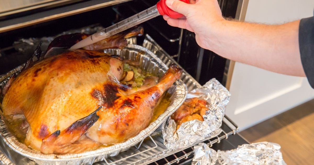A person basting a turkey in the oven.