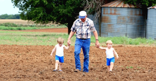 A grandfather holdling hands with his two grandchildren in a field