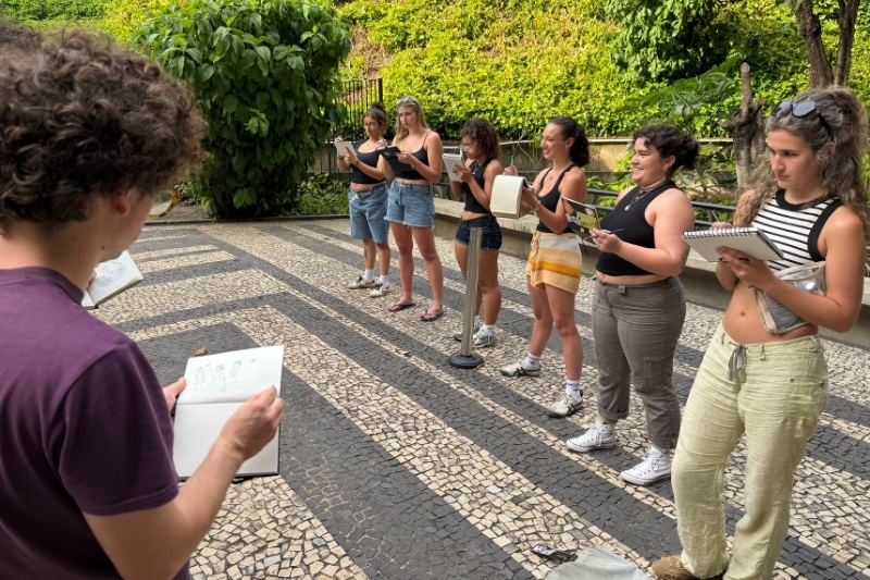 Students stand in a line sketching in their notebooks.