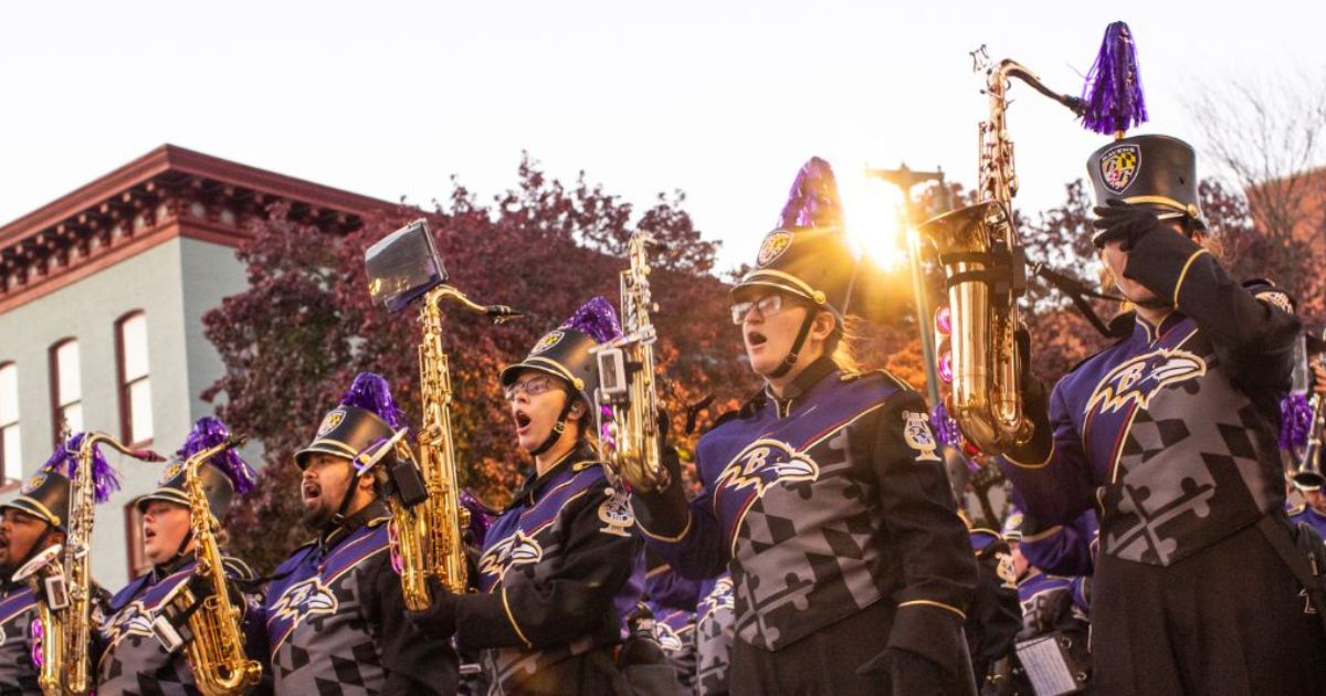 People stand in a row in marching badn uniforms, holding up saxophones.