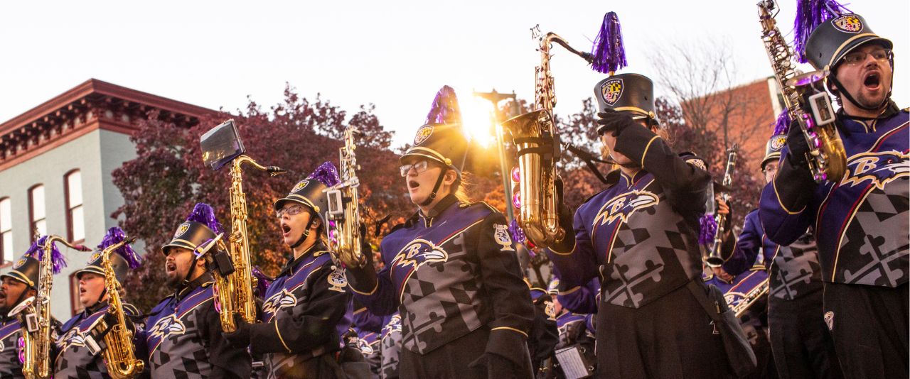 People stand in a line in marching band uniforms holding up saxophones.