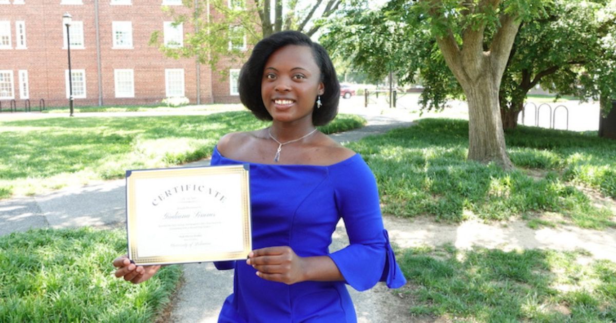 Rising junior Giuliana Simms is the 2025 winner of the Seitz Award. She holds up her award, standing in front of a tree and a building.
