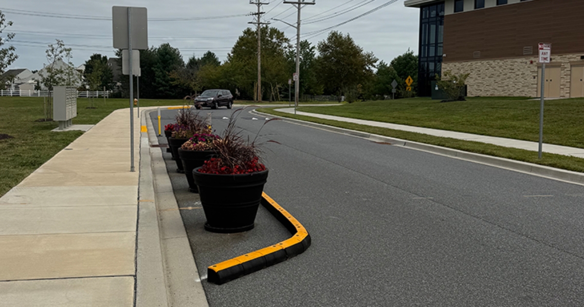 A street with planters on the left and a car in the background.