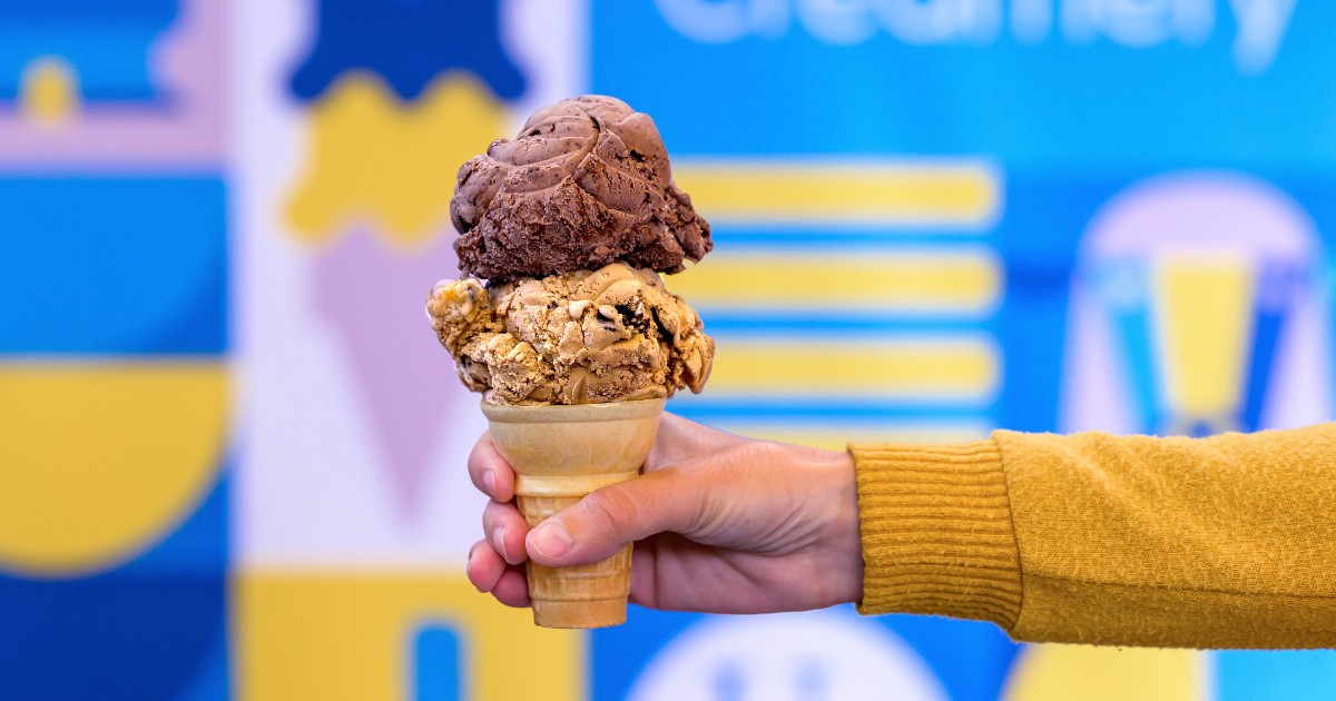 A hand holds an ice cream cone with two scoops of ice cream.