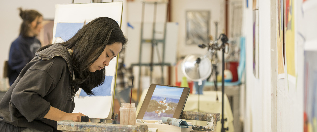CAS student learning about beginning oil painting methods in an art studio with a canvas in the background.
