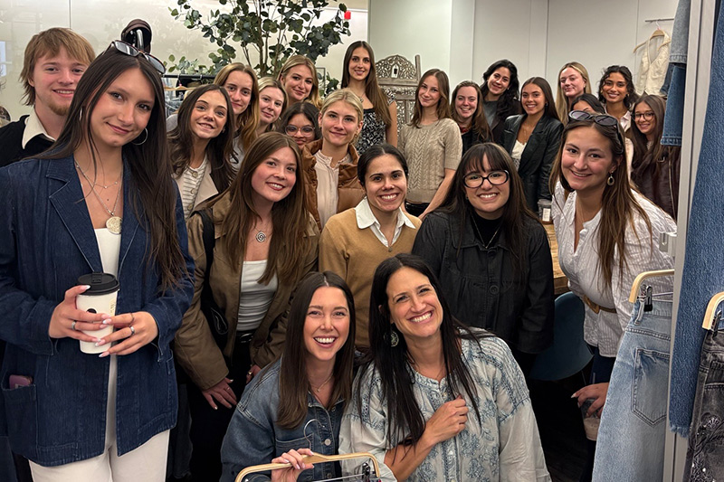 Image 2: Fashion design students and faculty gather for a group photo inside a clothing showroom.