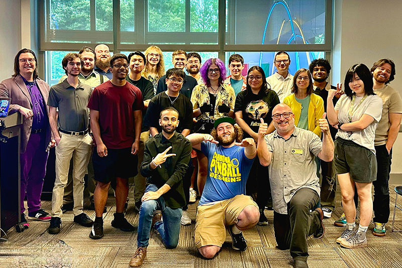 A group of University of Delaware students and instructors pose together in front of a large window after a Game Studies and Esports event.