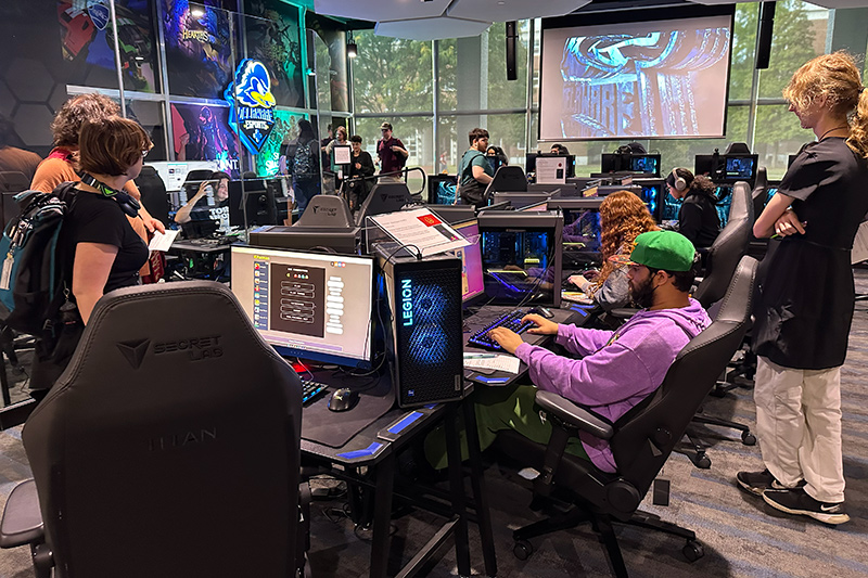 Students use gaming computers in the University of Delaware esports lab, with large monitors and gaming equipment throughout the room.