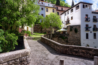 An old stone street lined on either side with a stone wall that winds uphill through a historic neighborhood of white stucco buildings in Granada Spain.