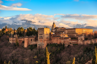 9th century castle on top of a mountain, surrounded by trees, mountains and puffy white clouds.