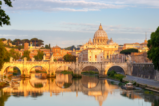 Golden sunrise light over Saint Peter's Cathedral with a river and ancient Roman bridge in the foreground.