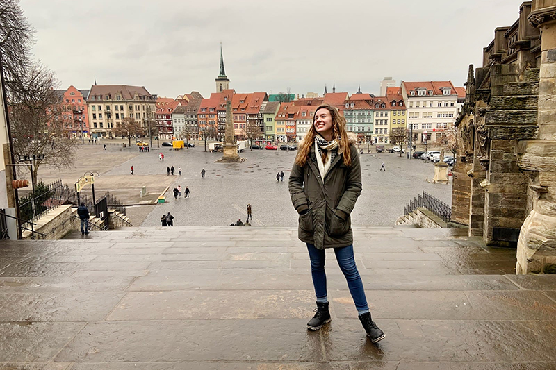 University of Delaware student Rachel Harell stands on stone steps of a historic building overlooking a city square in Leipzig, Germany.
