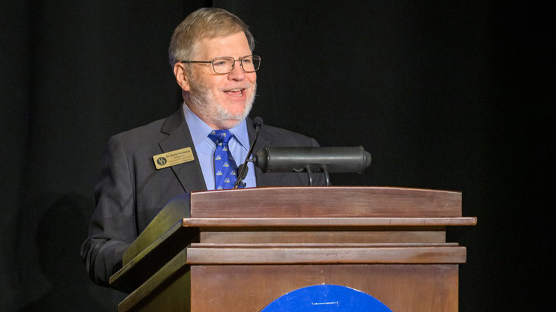 A college professor delivers remarks from a podium.