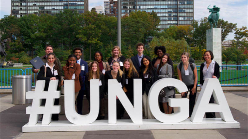 A group of college students in business attire gather behind a #UNGA monument outside the United Nations in New York City.