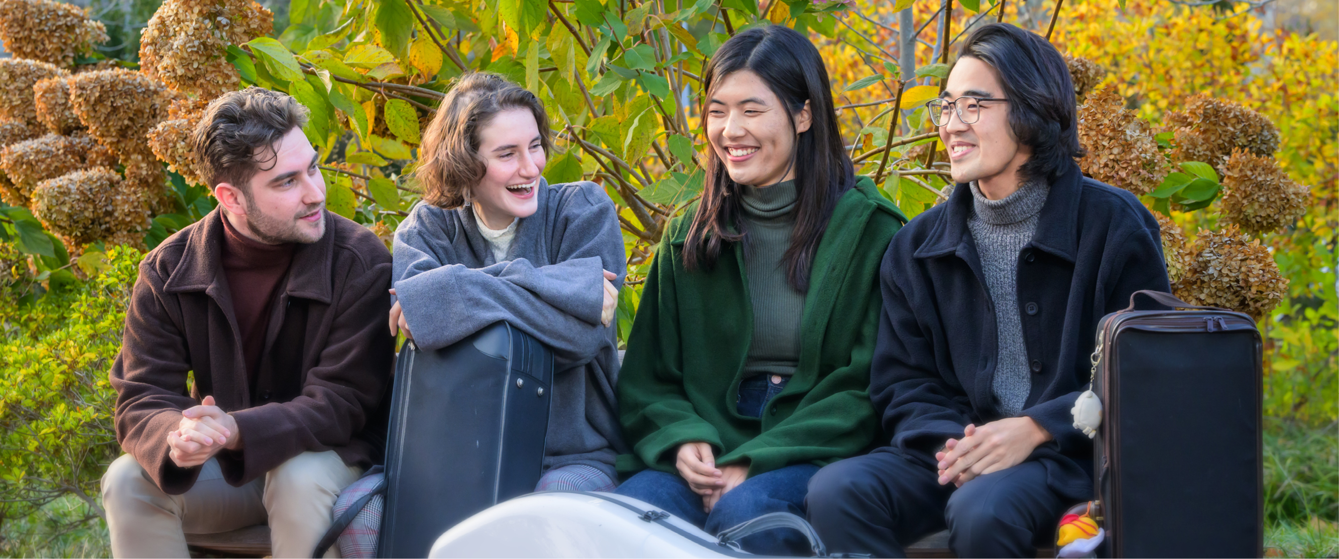 Four students sitting together laughing in front of fall foliage Four students sitting together laughing in front of fall foliage