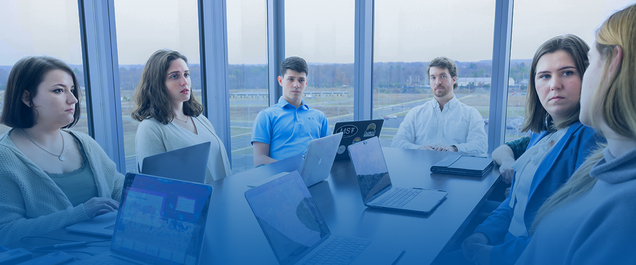 A group of professionals meet around a conference table with their laptops.