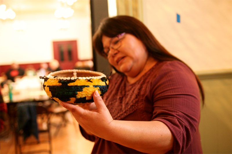 A woman holds up a small yellow and black woven basket.