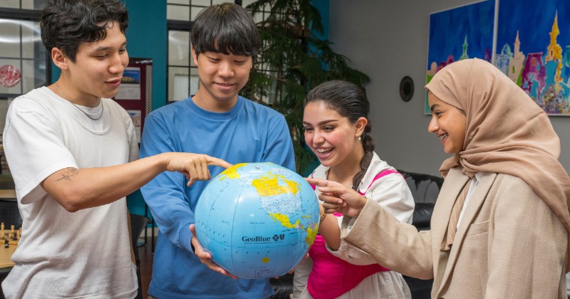 Four students pointing at a globe