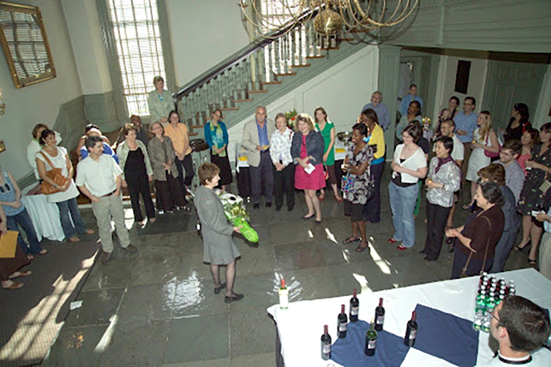 A zoomed out view from above of a group of smiling people attending a party inside a historic academic building.