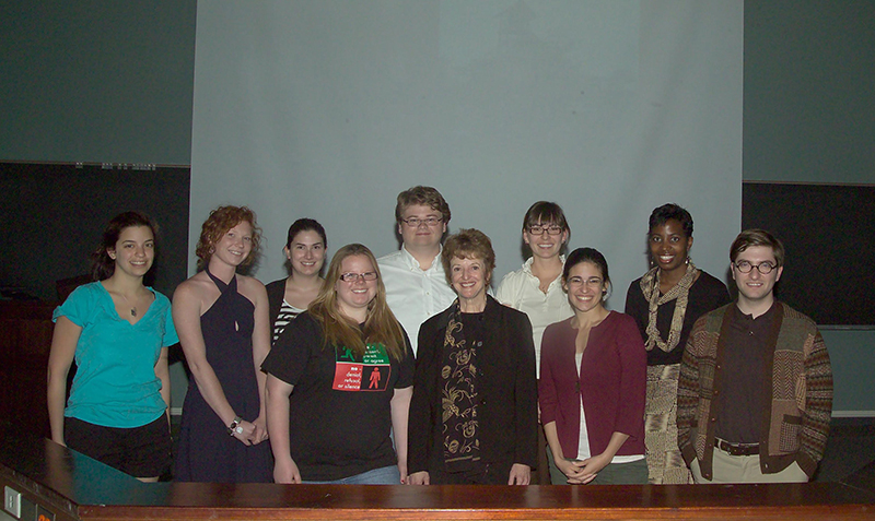 Smiling students and faculty in group photo inside a college lecture hall. 