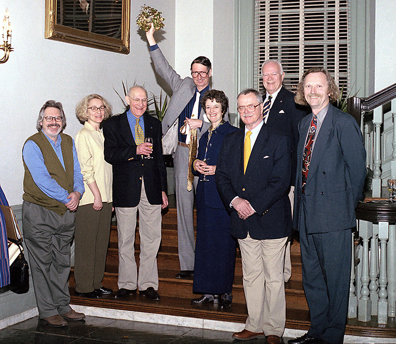 A group of smiling people dressed in business attire stand on the steps inside a historic building for a group photo.