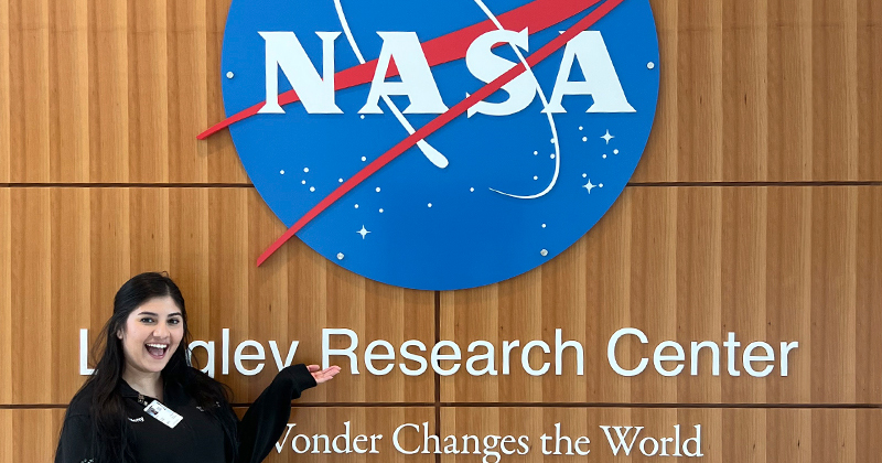 Yuleny Gomez Rodriguez stands next to the NASA logo on the wall of the NASA Langley Research Center.