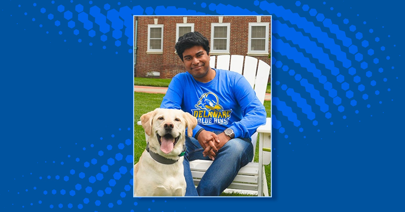 A college student and a white labrador retriever sit together on the The Green at the University of Delaware.
