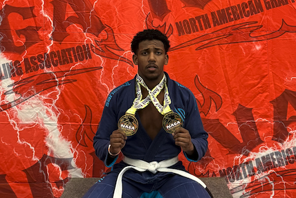 Mohammed Alharbi holds up two awards around his next while wearing a jiu-jitsu uniform after a competition.