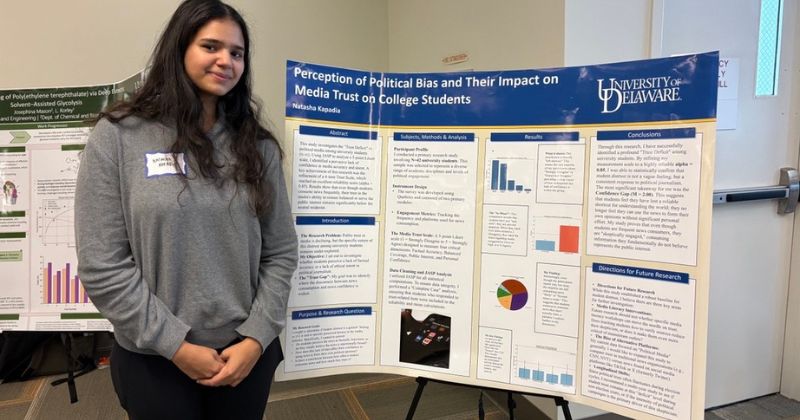 A college student stands next to a poster presentation of her research.