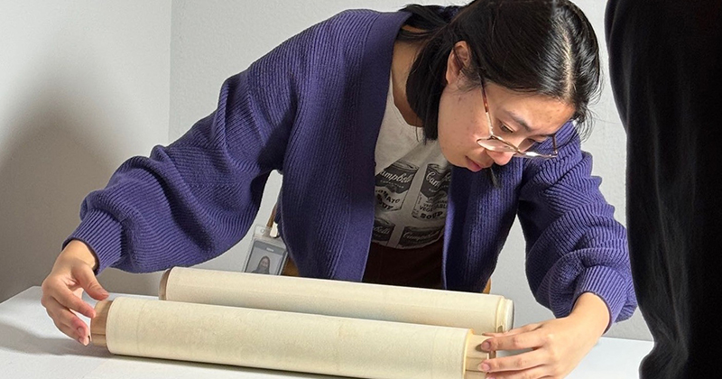 College student carefully handles a scroll at a museum.