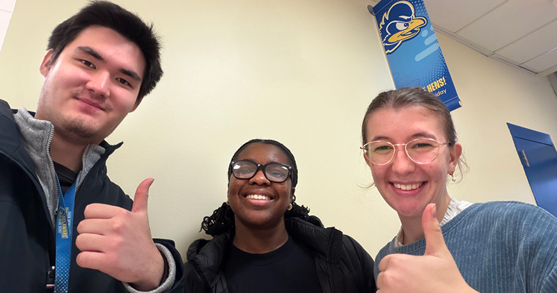 Three smiling college students give a thumbs up