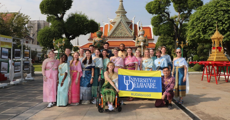 A group of smiling students and chaperones gather for a group photo in front of a temple in Thailand.