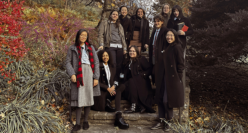 A group of 10 graduate students wearing coats gathered for a group photo on sunny fall day.