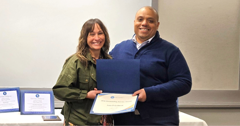 Two smiling people holding an award certificate. 