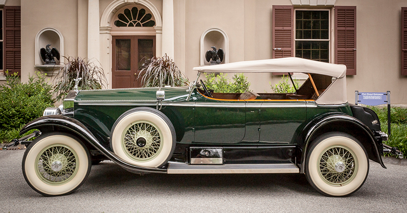 A green 1927 Rolls Royce parked in front of a historic house. 
