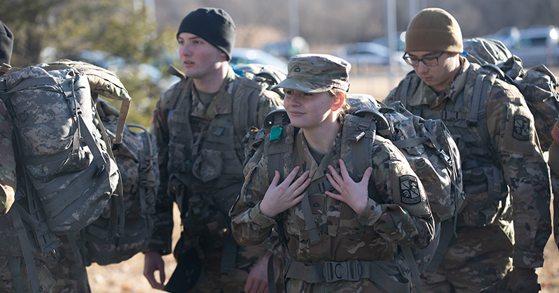 Army ROTC cadets marching in fatigues with backpacks.