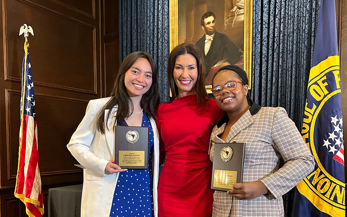 A college professor stands between two students holding award plaques