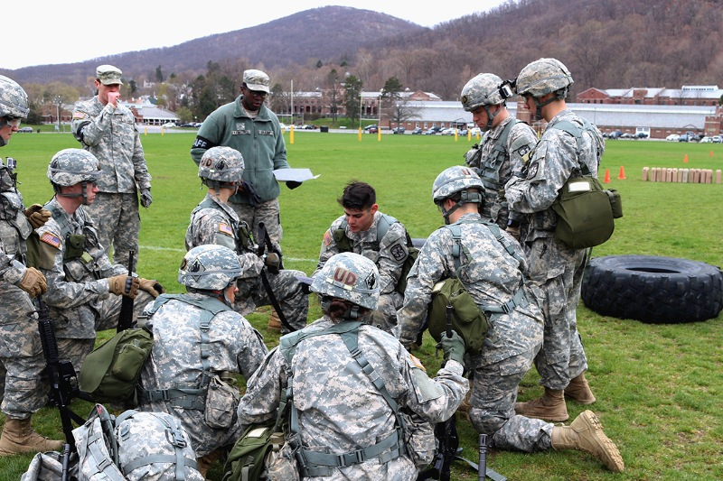 ROTC members at the University of Delaware in uniform on an open green field kneeling