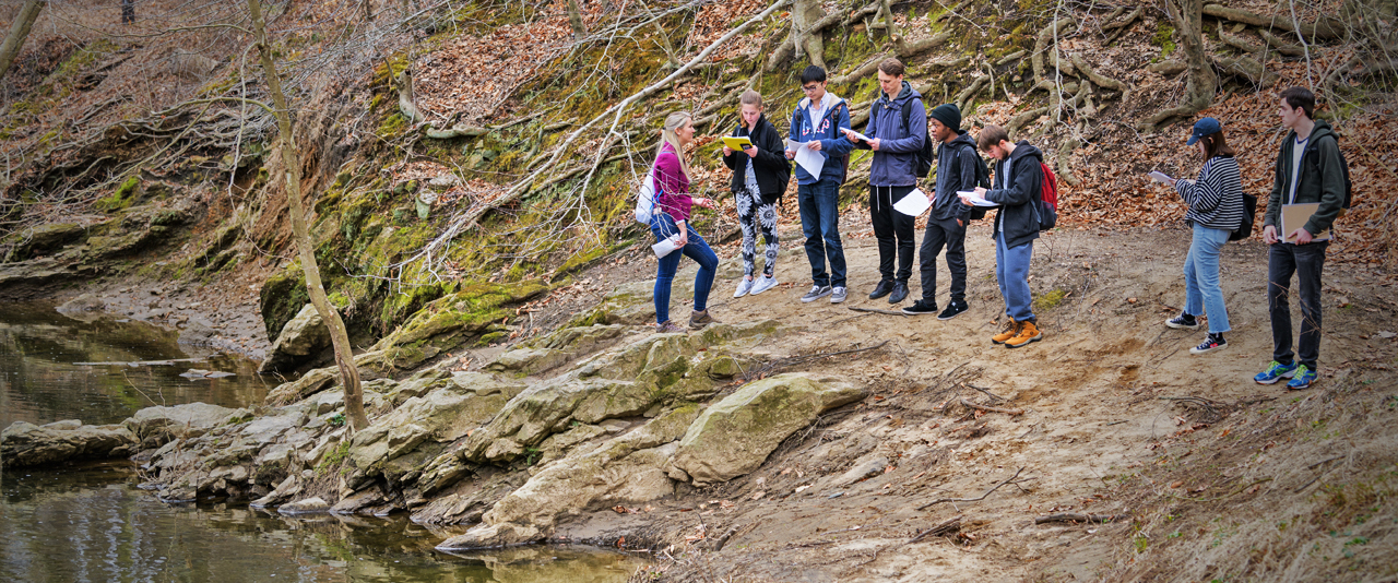 Group of students examines creek formations during an outdoor excursion in a earth sciences class