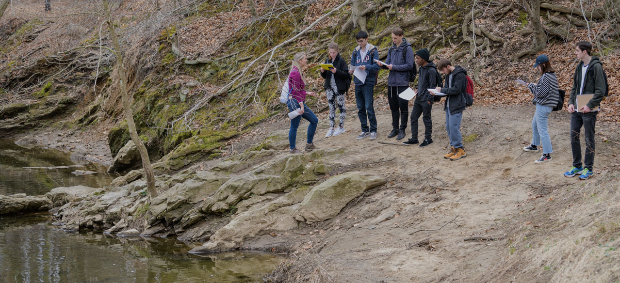 Group of students examines creek formations during an outdoor excursion in a earth sciences class