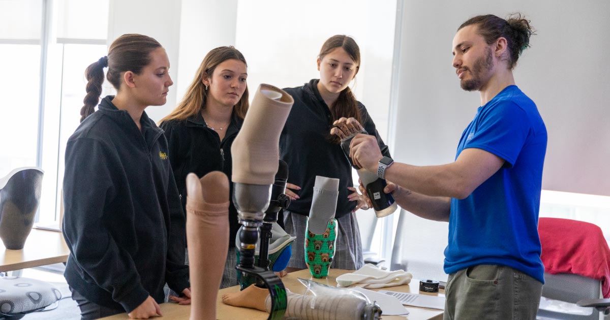Three female high school students examine a leg replica that a college student is showing as part of Biomechanics Day