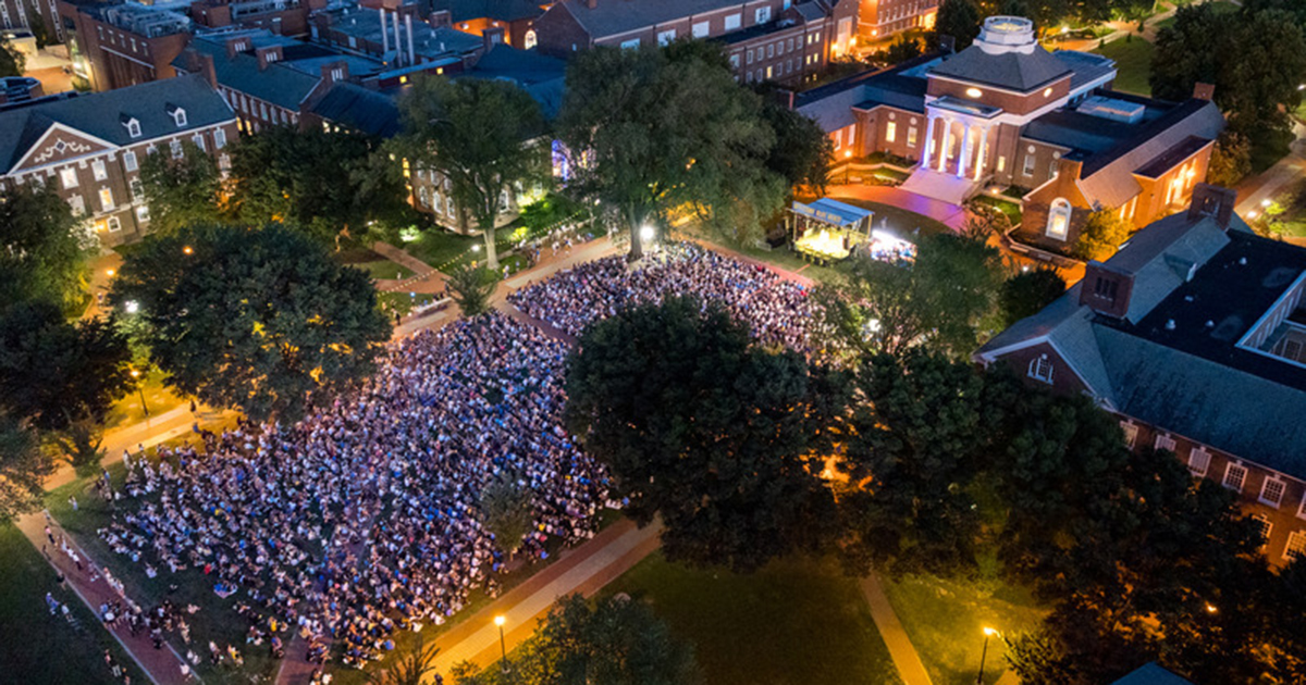 An overhead shot taken at night with students standing shoulder to shoulder packing The Green, each holding a candle to light up The Green.